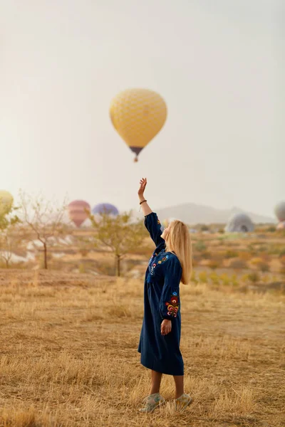 Mujer hermosa tratando de alcanzar globo de aire caliente en el cielo con la mano —  Fotos de Stock