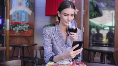 Şarap içme ve telefonunuzun ve restoranda gülümseyen kadın