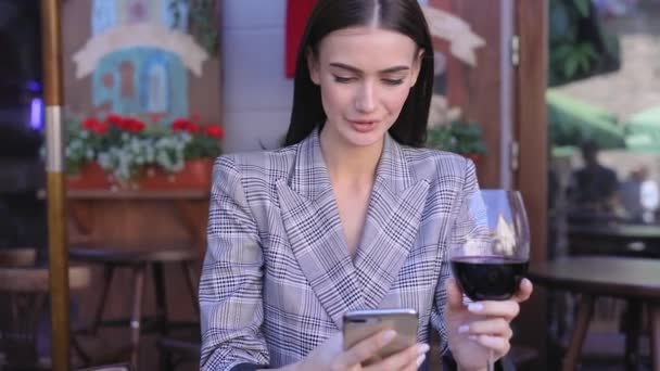 Усміхнена жінка п'є вино і використовує телефон в ресторані — стокове відео