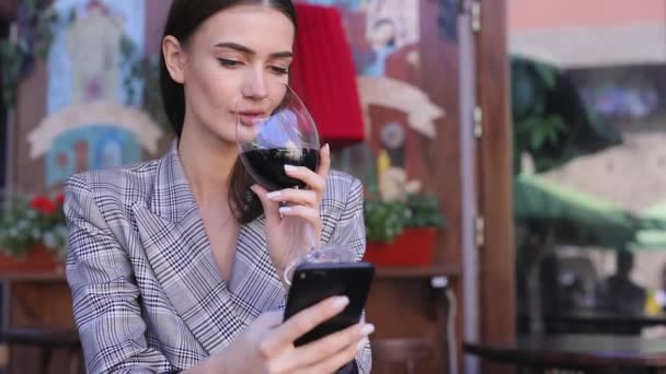 Mujer sonriente bebiendo vino y usando el teléfono en el restaurante — Vídeo de stock