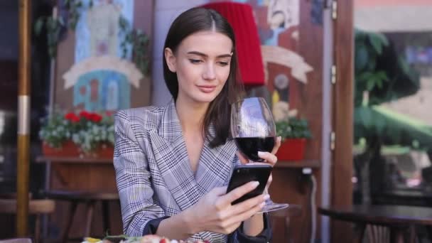 Leende kvinna dricker vin och använder telefonen på restaurang — Stockvideo