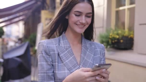 Hermosa mujer sonriente usando teléfono caminando en la calle de la ciudad — Vídeo de stock