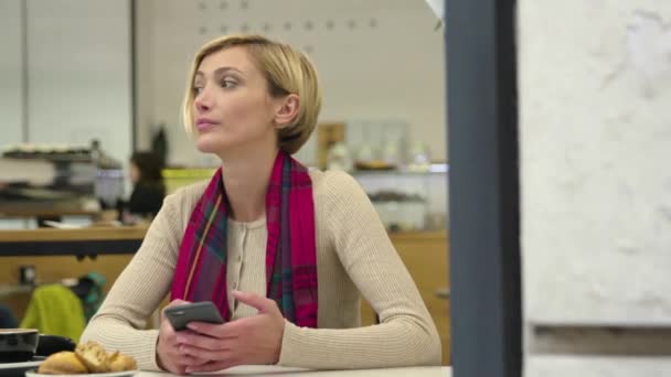 Жінка з мобільним телефоном чекає на столі в кафе — стокове відео