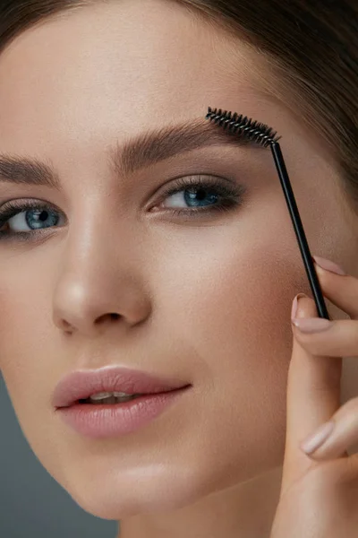 Wenkbrauw make-up. Vrouw poetsen wenkbrauwen met gel borstel close-up — Stockfoto