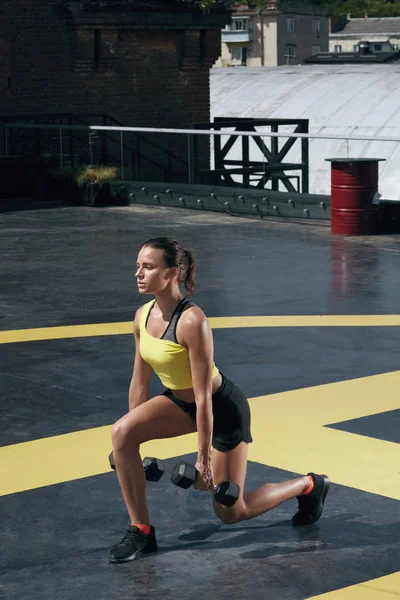 Тренировка. Женщина делает упражнения для ног с гантелями на свежем воздухе — стоковое фото