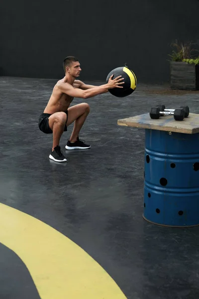 Ejercicio. Hombre de deporte haciendo ejercicio en cuclillas con pelota médica en el gimnasio —  Fotos de Stock