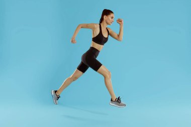 Uygun vücut atlama ve mavi arka plan üzerinde çalışan spor kadın
