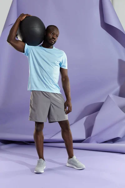 Спортсмен у спортивному одязі з медичним м'ячем на фіолетовому фоні — стокове фото