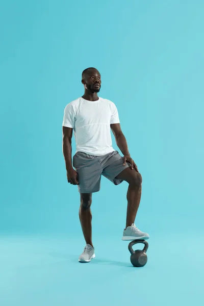 Uomo sportivo in abbigliamento sportivo con kettlebell su sfondo blu — Foto Stock