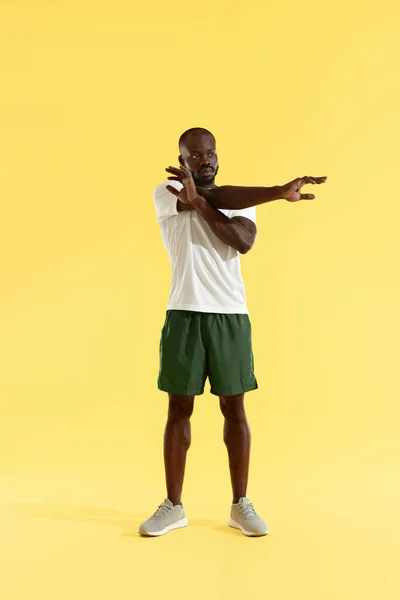 トレーニング。腕を伸ばす男、黄色の背景にウォーミングアップ — ストック写真