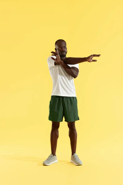 Entrenamiento. Hombre estirando el brazo, calentando sobre fondo amarillo — Foto de Stock