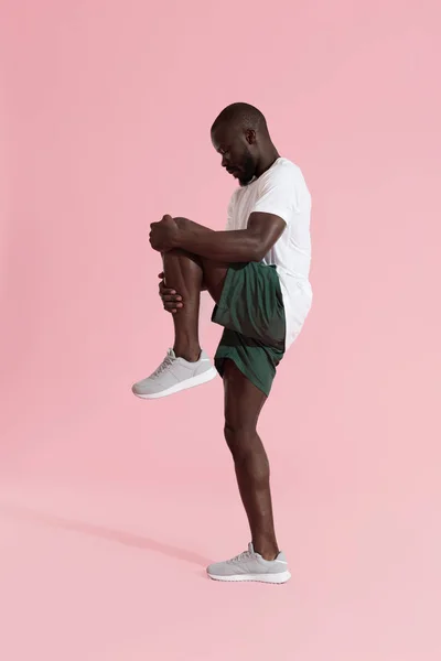 Hombre en ropa deportiva que estira las piernas, calentándose sobre fondo rosa — Foto de Stock