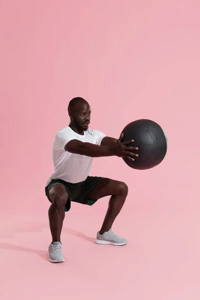 Entrenamiento. Hombre deportivo haciendo ejercicio, haciendo sentadillas con pelota médica — Foto de Stock