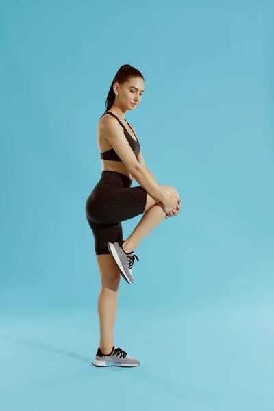 Фитнес. Женщина в спортивной одежде растягивает ноги на синем фоне — стоковое фото