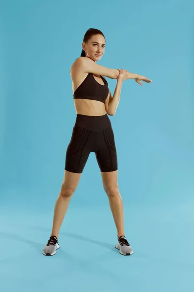 Fitness. Mujer estirando el brazo, calentando sobre fondo azul — Foto de Stock