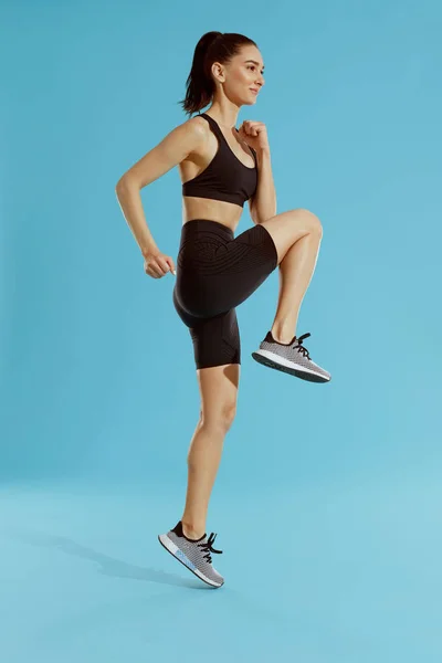 Fitness workout. Woman exercising, jumping on blue background — Stock Photo, Image