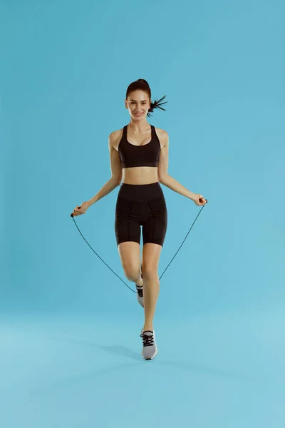 Fitness. Woman exercising with jumping rope on blue background — Stock Photo, Image