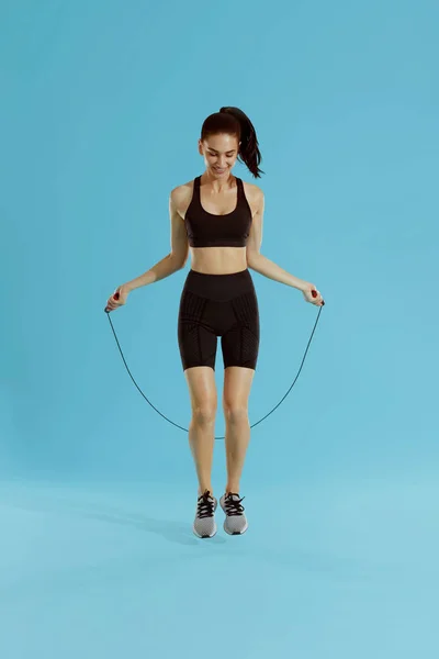 En forme. Femme faisant de l'exercice avec corde sautante sur fond bleu — Photo