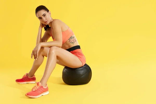 Mulher fitness em esportes desgaste na bola med no fundo amarelo — Fotografia de Stock