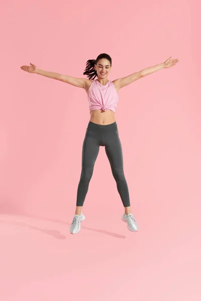 Salto de fitness. Mulher fazendo exercício de salto no fundo rosa — Fotografia de Stock