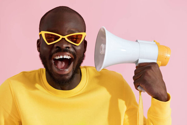 Счастливый черный мужчина в модных солнцезащитных очках с мегафоном смеется
 