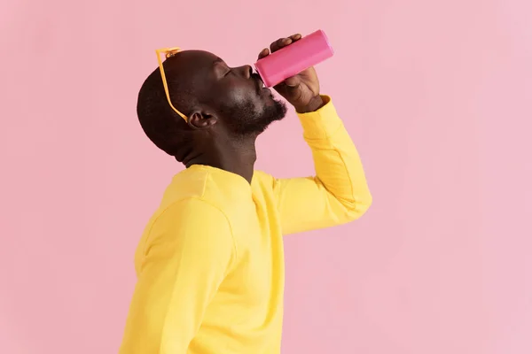 Minumlah. Pria kulit hitam minum minuman ringan pada potret latar belakang merah muda — Stok Foto