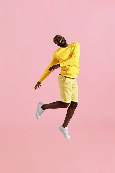 Salta. Feliz hombre negro saltando en el aire riendo sobre fondo rosa — Foto de Stock