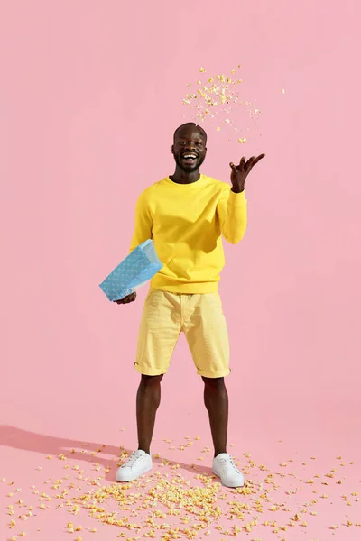 Happy black man having fun throwing pop corn in air