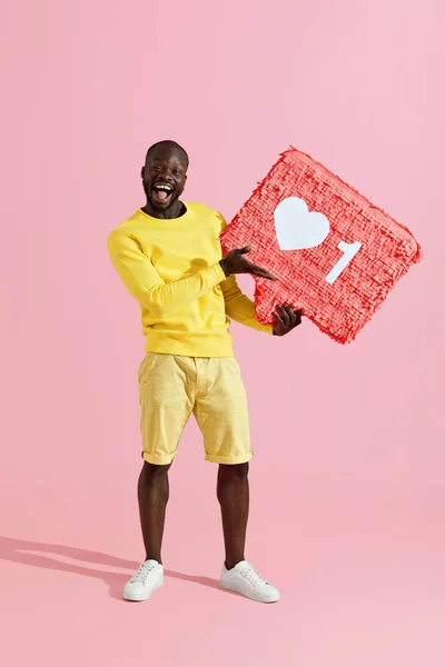 Like. Happy black man holding like heart icon pinata on pink