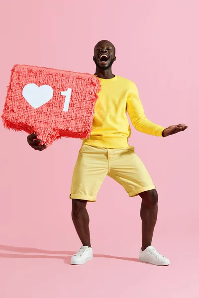 ¿Cómo? Feliz hombre negro sosteniendo como corazón icono de piñata en rosa — Foto de Stock