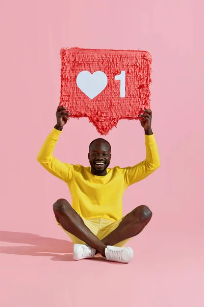 Like. Happy black man holding like heart icon pinata on pink
