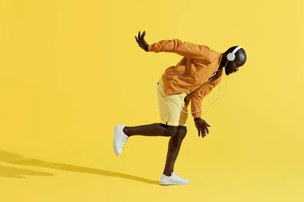 Hombre con auriculares escuchando música, bailando sobre fondo amarillo — Foto de Stock