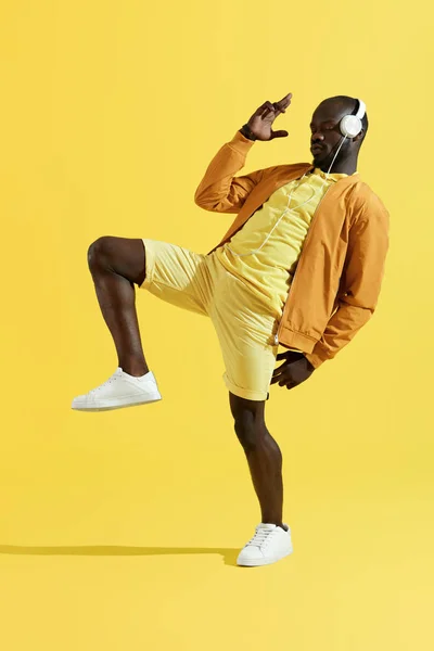 Hombre con auriculares escuchando música, bailando sobre fondo amarillo — Foto de Stock