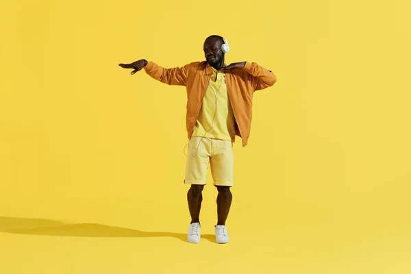 Hombre con auriculares escuchando música, bailando sobre fondo amarillo — Foto de Stock