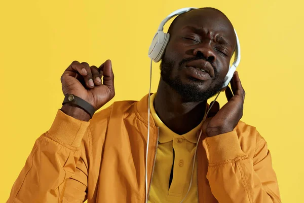 黄色の背景で歌う、音楽を聴くヘッドフォンの男 — ストック写真