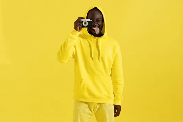 Szczęśliwy człowiek w kolorowych ubrań z aparatem fotograficznym na żółtym — Zdjęcie stockowe