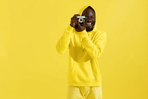Szczęśliwy człowiek w kolorowych ubrań z aparatem fotograficznym na żółtym — Zdjęcie stockowe