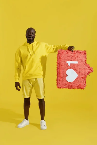 ¿Cómo? Feliz hombre negro sosteniendo como corazón icono de piñata en amarillo — Foto de Stock