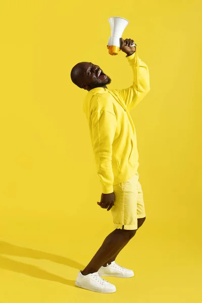 Atenção! Homem negro gritando em megafone no fundo amarelo — Fotografia de Stock