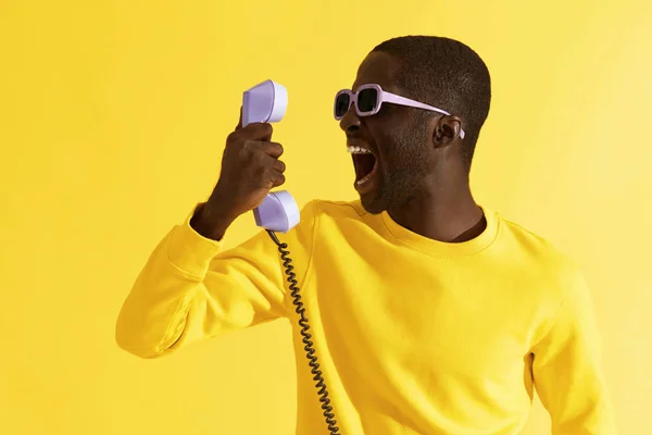 Schwarzer Mann mit Sonnenbrille schreit am Telefon auf gelbem Hintergrund — Stockfoto