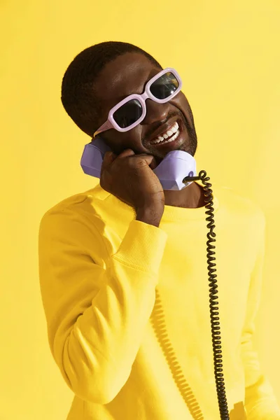 Retrato hombre feliz en gafas de sol con teléfono sobre fondo amarillo — Foto de Stock