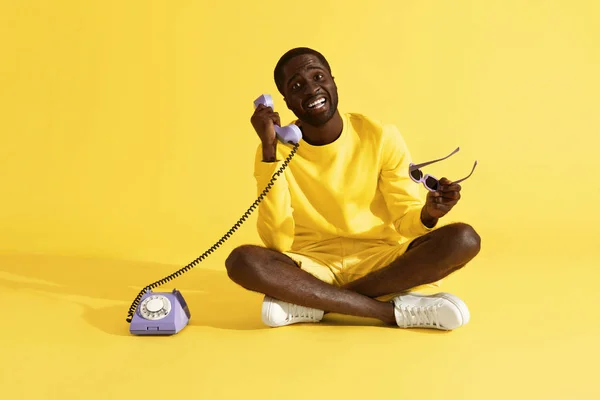 Šťastný muž, který mluví na purpurovém telefonu, sedí na žlutém pozadí — Stock fotografie