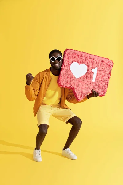 Hombre sonriente con icono, piñata de corazón sobre fondo amarillo — Foto de Stock