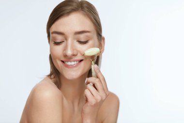 Yüz masajı. Cilt bakımı için yeşim rulo kullanarak Gülümseyen kadın