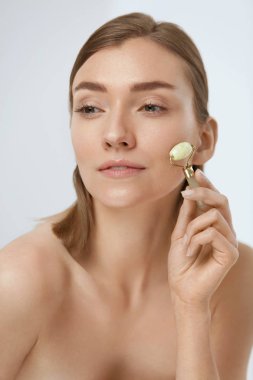 Yüz masajı. Güzellik tedavisi için yeşim rulo kullanan kadın