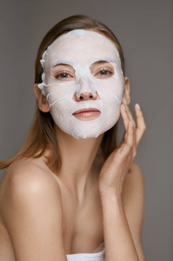 Yüz maskesi. Spa bakımı için yüz derisinde çarşaf maskesi kullanan kadın
