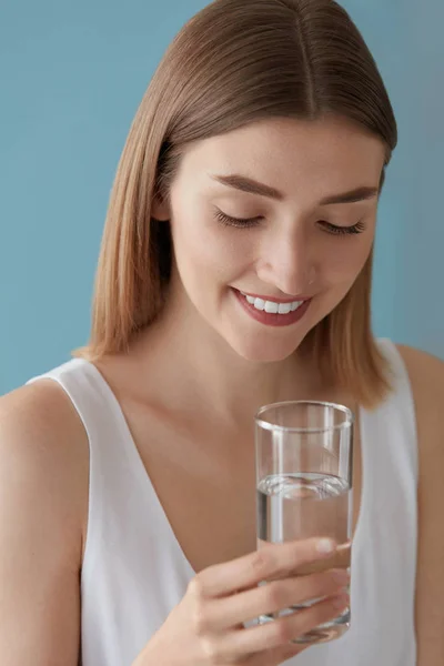 Lachende vrouw met glas water binnenshuis staand — Stockfoto