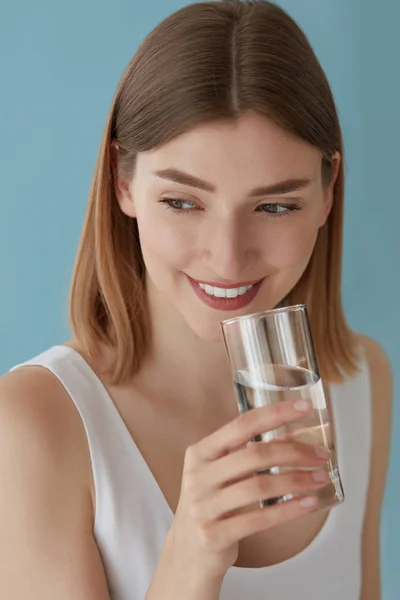 Lachende vrouw met glas water binnenshuis staand — Stockfoto