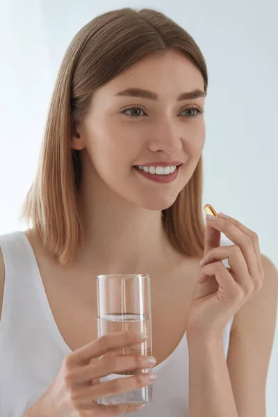 Mulher tomando pílula vitamínica com copo de água doce dentro de casa — Fotografia de Stock