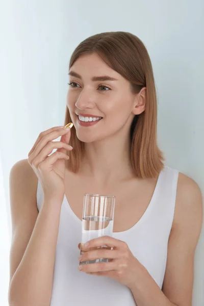 Mulher tomando pílula vitamínica com copo de água doce dentro de casa — Fotografia de Stock